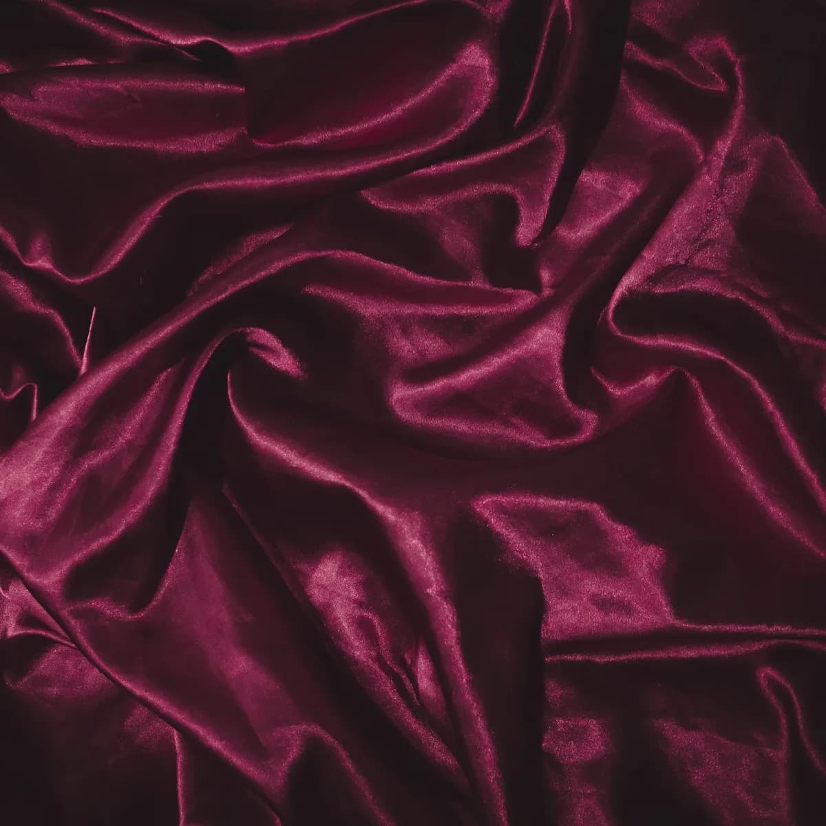 Folds of deep burgundy satin lit from one side against black.
