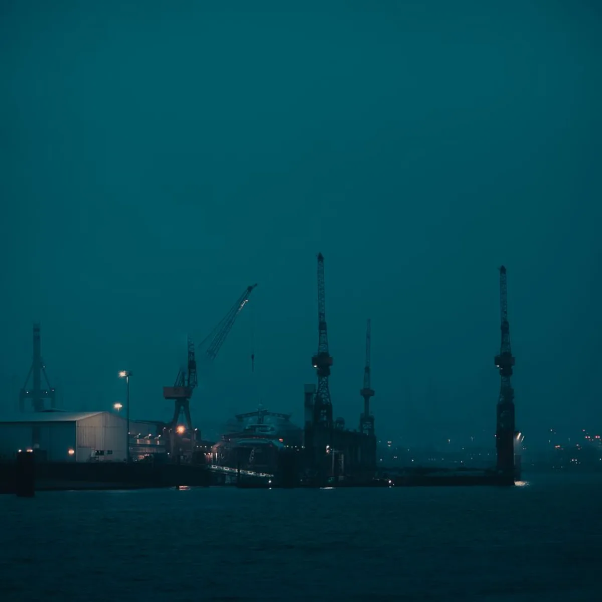 Harbour cranes fading into thick morning fog.