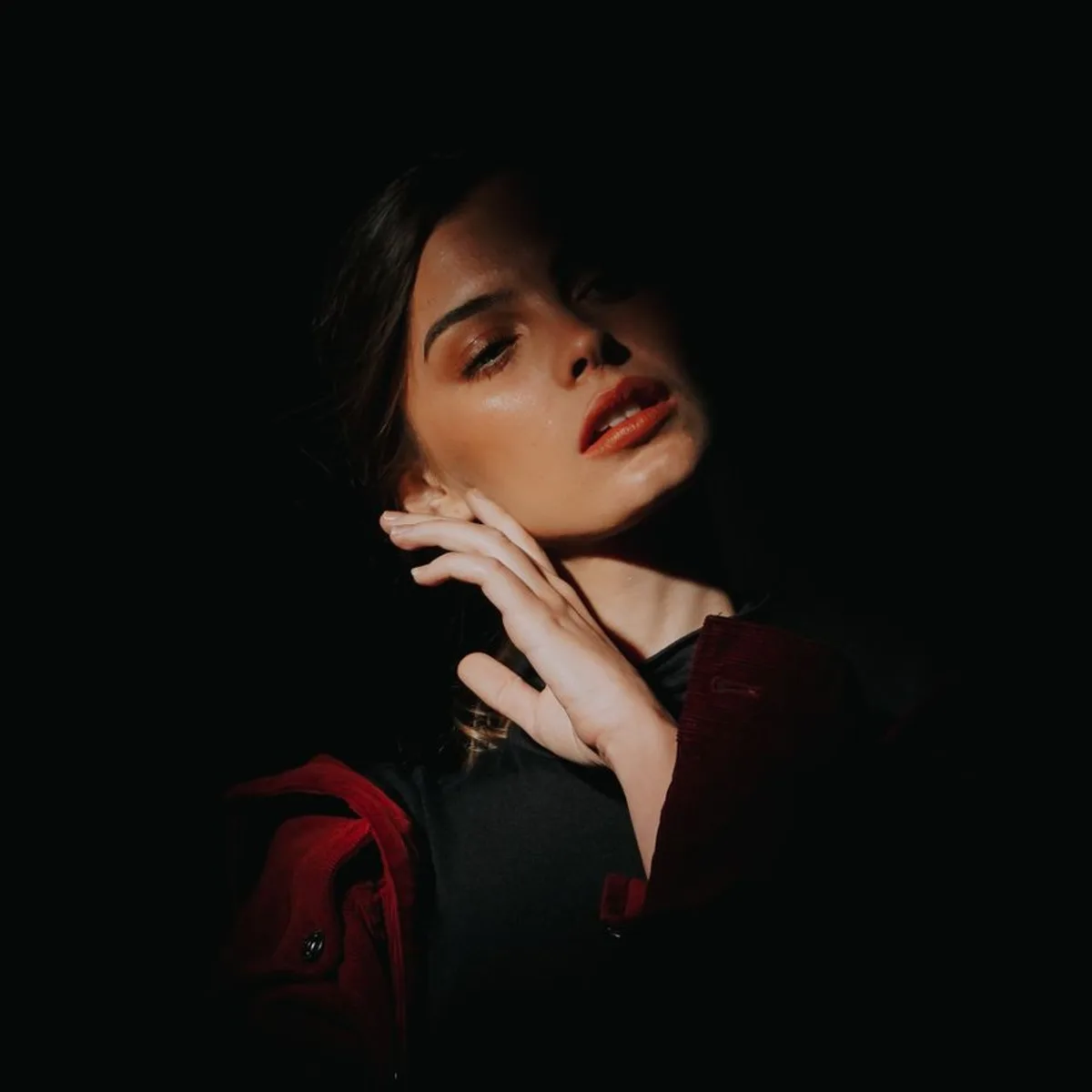 Editorial portrait of a woman in black, lit from one side against a dark ground.