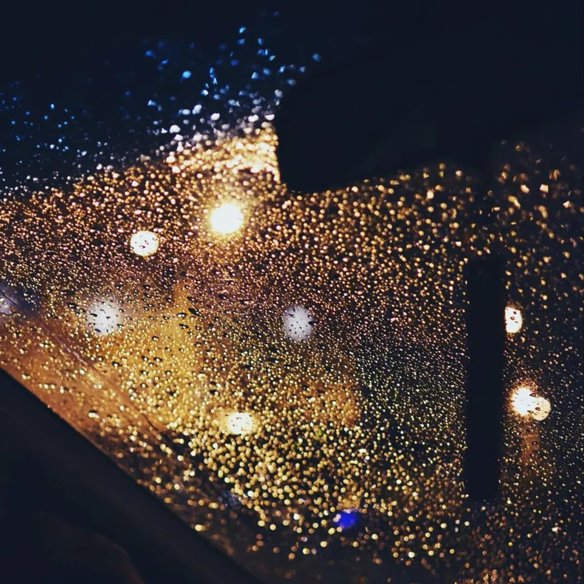 Rain beading on a windscreen with night traffic out of focus behind.